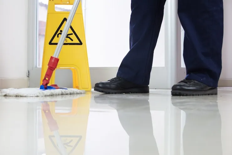 low-angle-closeup-person-cleaning-floor-with-mop-near-yellow-caution-wet-floor-sign_181624-37077